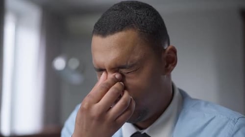 Closeup Portrait of Tired African American Young Man Rubbing Eyes Working in Home Office on Covid19