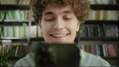 Handsome Curly Student Man Holding Modern Smartphone Texting Message in Home Office or Library