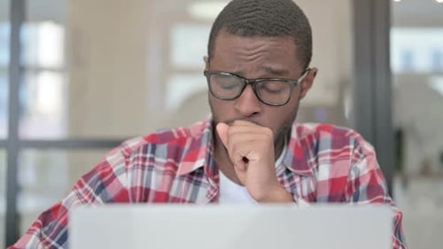 Close Up of African Man Coughing While Using Laptop