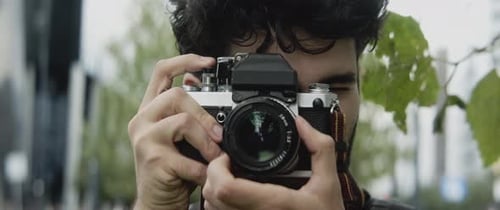 Young Man Taking Photo with Vintage Camera in City
