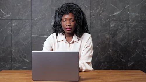 AfricanAmerican Woman with Headphones at Video Chat By Wall