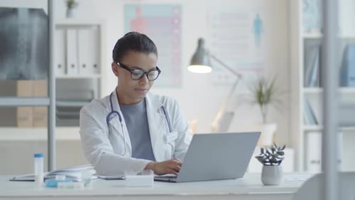 Doctor Works on Laptop Then Smiles at Camera