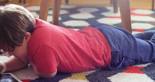 Child Lies on Rug Playing on Tablet