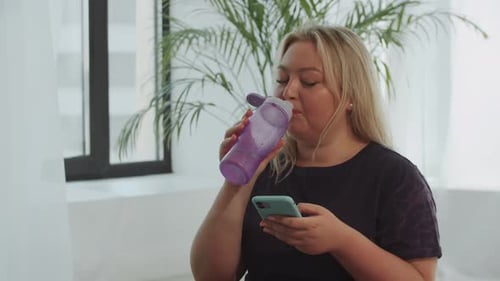 Young Woman Using Phone, Drinking Water Indoors