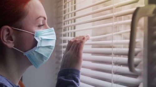 Young Adult in Mask Looking Out Window