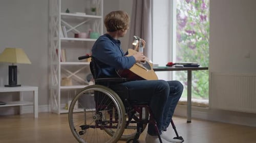 Side View Portrait Talented Disabled Caucasian Man Playing Guitar Sitting in Wheelchair at Home