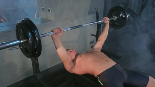 Man Bench Pressing Weights in Gym with Smoke