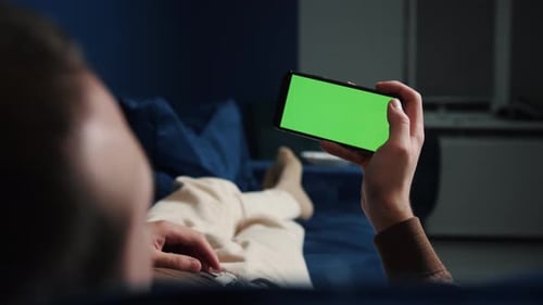 Man Lying on Couch Using Smartphone with Chroma Key Green Screen at Night, Through Social Media