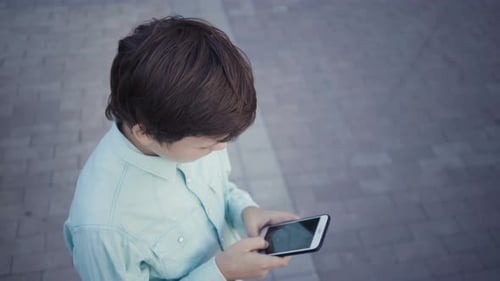 Boy Using Mobile Phone on Urban Sidewalk