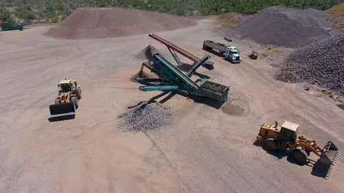 Wide drone shot of an excavators loading rocks on a conveyer belt in a rock quarry