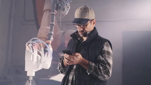 Male Artisan Using Smartphone Near Robotic Arm
