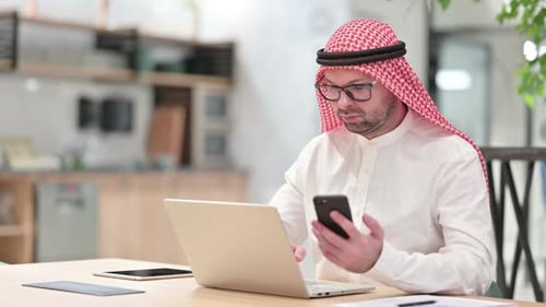 Professional Young Arab Businessman Using Smartphone and Laptop in Office