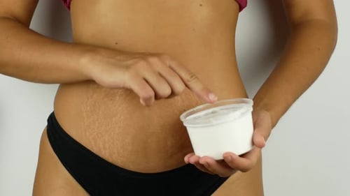 Schönes Mädchen schmiert ihren Bauch mit Sahne. Empfindliche Handmassage. Eine Frau nach der Geburt