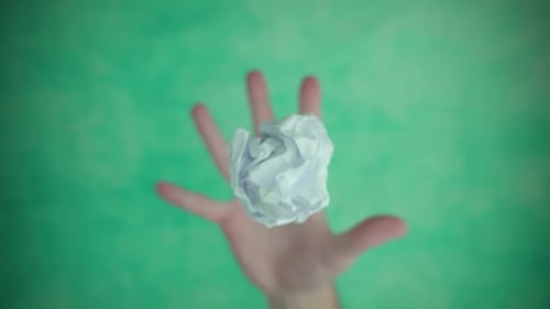 Mano que lanza y atrapa la bola de papel sobre la superficie verde