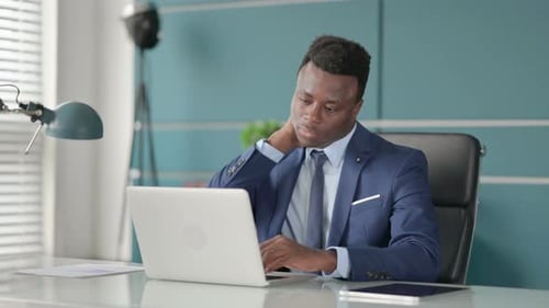 African Businessman Having Neck Pain While Using Laptop in Office