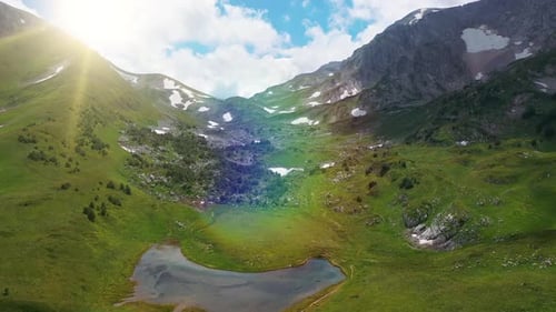 Aerial View with Approaching Mountain Covered with Dense Green Grass, Snow with Small Lake of Stones