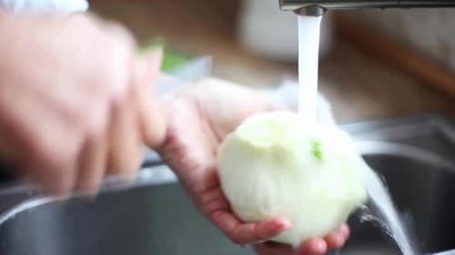Frau wäscht Fenchelknolle unter fließendem Wasser