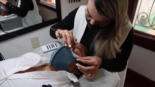 Crop cosmetologist applying patch on face of black woman