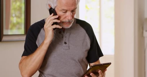 Mature Man Holding Tablet Talking on Cellphone