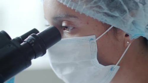 Close Up of Female Lab Worker in Medical Mask and Hat Using Microscope