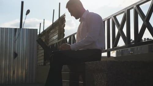 Young Businessman Works on Notebook Sitting on Bench at City