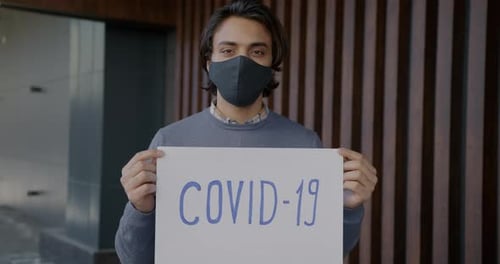 Person Holds COVID-19 Sign While Wearing Face Mask