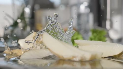 Fatias de batata não cozidas e com casca caem no prato com água. - de perto, câmera lenta