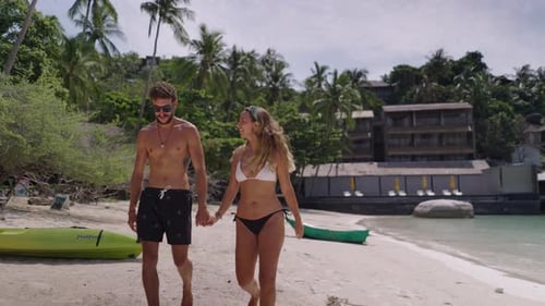 A Side View of a Young Couple Walking on Beach Near Sea