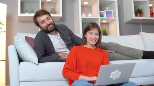 Woman Works on Laptop with Man on Sofa