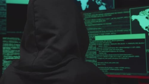 Back View Of Hacker Hacking With Multiple Computer Screens In Dark Room