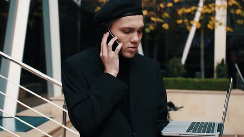 Caucasian Businessman Talking on Phone While Working on Laptop Outside Office
