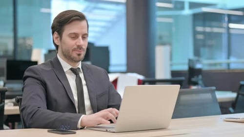 Businessman Showing Thumbs Up Sign While Using Laptop in Office