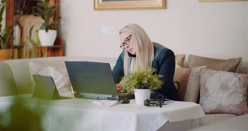 Businesswoman Working on Laptop on a Project at Home Office While Talking on Mobile with Client