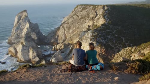 Couple of Backpack Tourists Sitting at Cliff