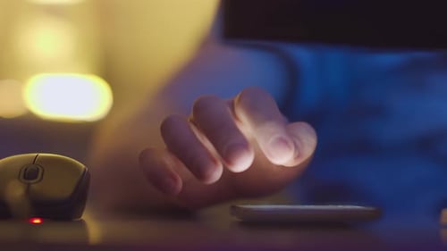 Man works at home on a computer and answers messages on his mobile phone, evening light