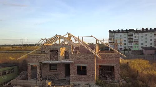 Aerial view of unfinished brick house with wooden roof structure under construction.