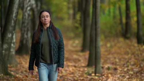 Adult Woman Is Walking Alone in Autumn Forest, Moving To Camera, Stepping Over Dry Foliage