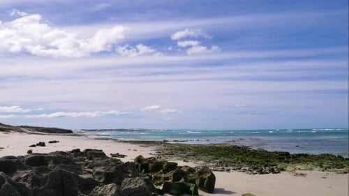 Timelapse - Cloudsing over white secluded beach with waves rolling in, rugged black rocks in foregro