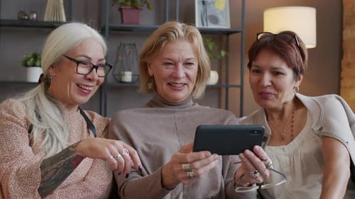 Drei erwachsene Freundinnen chatten beim Betrachten von Fotos auf dem Smartphone