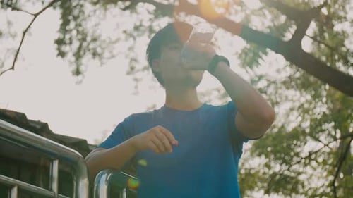 Asian sportsman drinking from a water bottle after workout running at the street in urban.