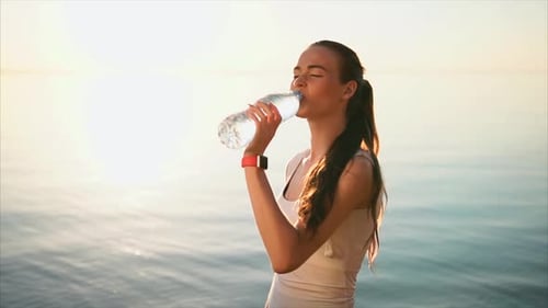 Young Sporty Woman Drinking a Water From the Plastic Bottle Near the Sea