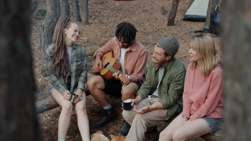 AfroAmerican Man Playing Guitar While Friends Tourists Singing and Laughing in Forest
