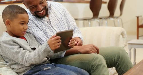 Father and Son Smiling at Tablet at Home