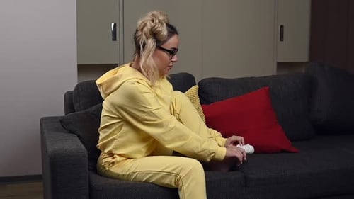 Woman Puts on Sock While Sitting on Sofa