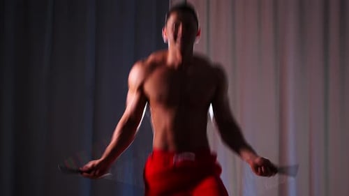 Sporttraining Athletischer muskulöser Mann ohne Hemd springt in Kontrastbeleuchtung über das Seil