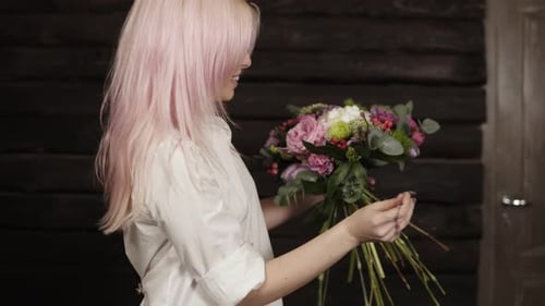 Une jeune femme aux cheveux roses réalise le dessin du bouquet en complétant la composition avec du saule