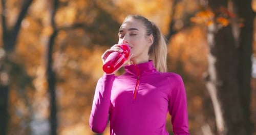Young Sporty Blonde Drinking Water During Jog Workout in Autumn Park