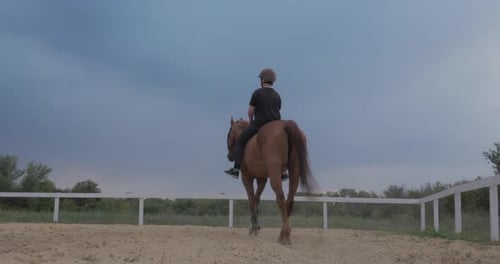 Person Riding Horse in Enclosed Sandy Paddock