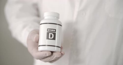Hand Holds Vitamin D Bottle in Medical Setting