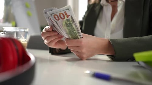 Person Counting Stacks of Money at a Desk